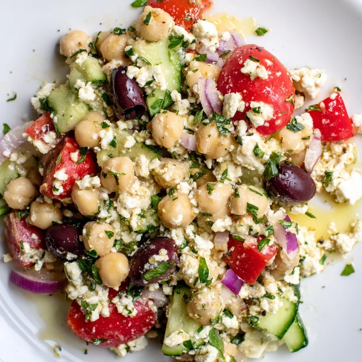 A close-up of Mediterranean Chickpea Salad in a white bowl, showcasing colorful cherry tomatoes, diced cucumbers, and crumbled feta cheese tossed with a bright lemon vinaigrette.