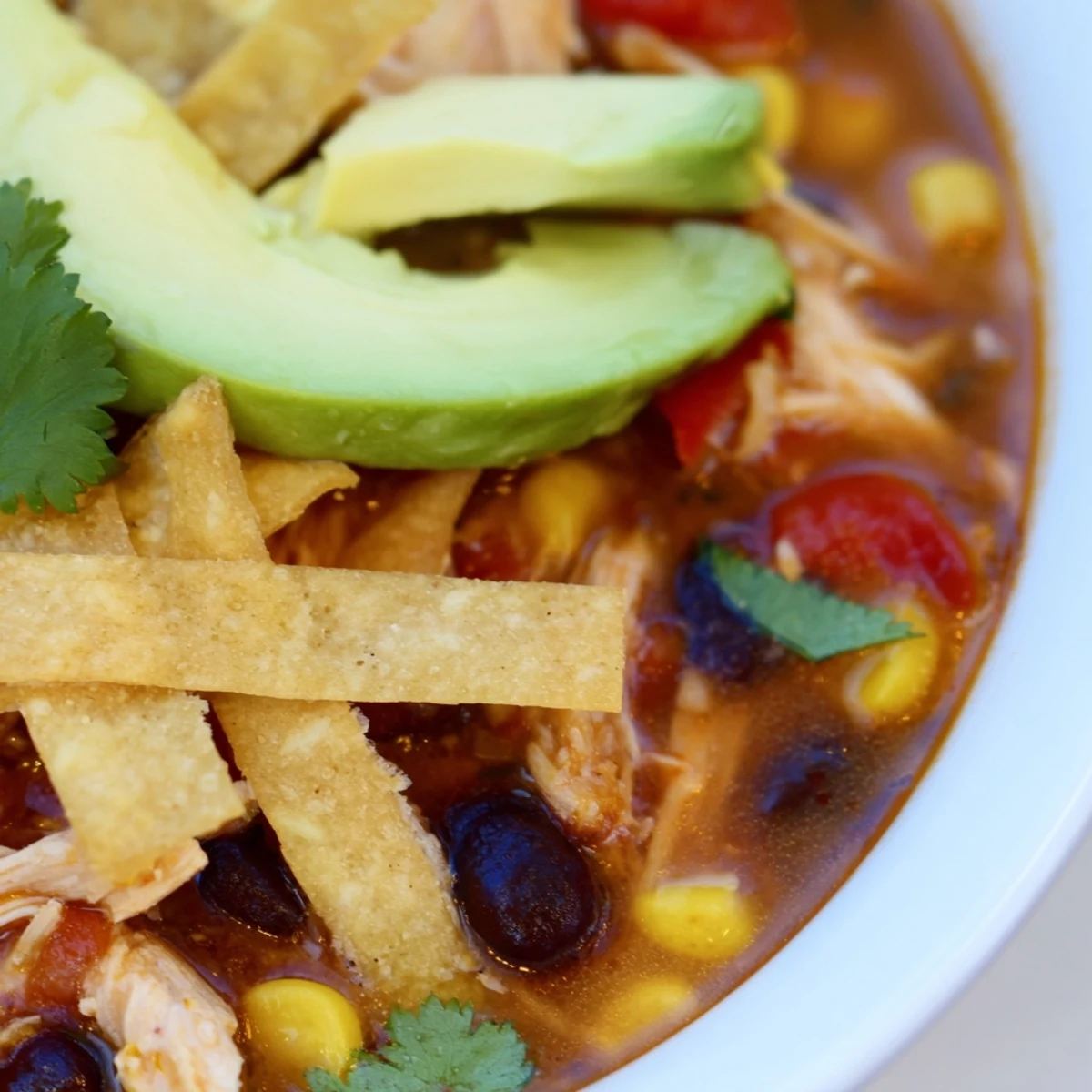 Steaming bowl of Chicken Tortilla Soup with Crispy Tortilla Strips, topped with avocado and cilantro.