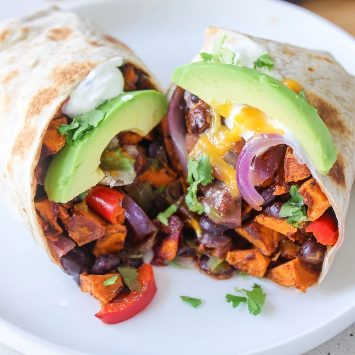 Four golden Roasted Sweet Potato and Black Bean Burritos are plated on a rustic table with lime wedges and fresh cilantro garnish.