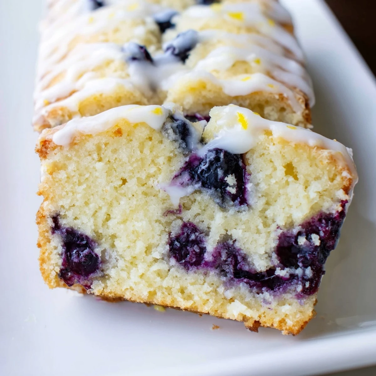 Sliced Lemon and Blueberry Yogurt Loaf showing tender cake with bursting blueberries, served on a white plate for a sweet morning treat.