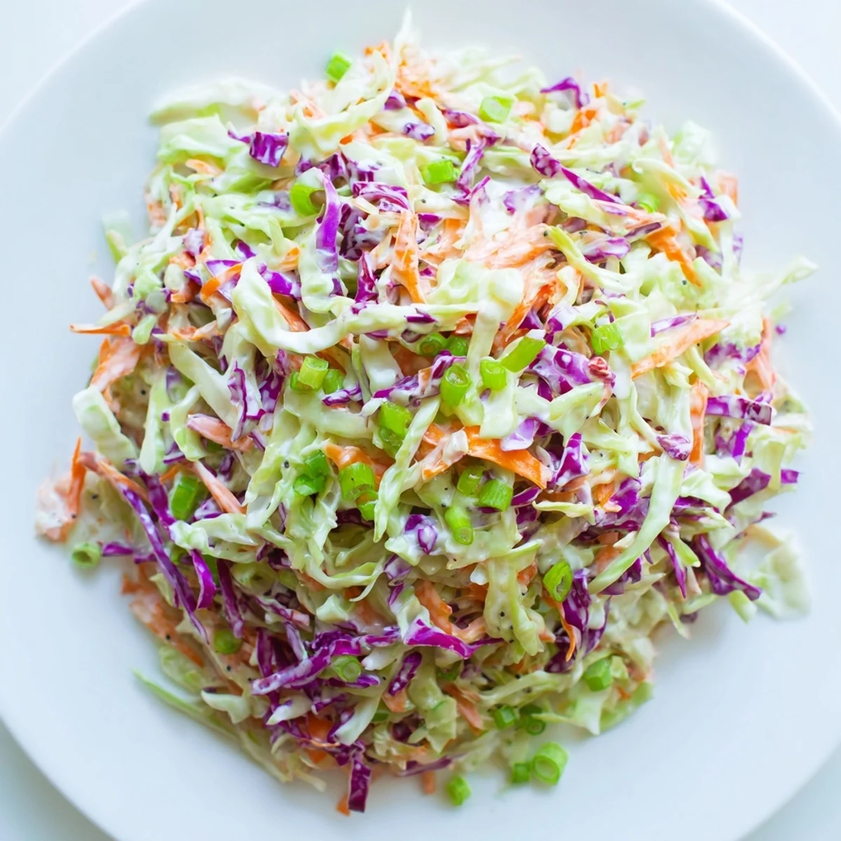 Creamy Coleslaw with Carrots in a chilled bowl garnished with green onions, highlighting the colorful mix of green and red cabbage shreds.