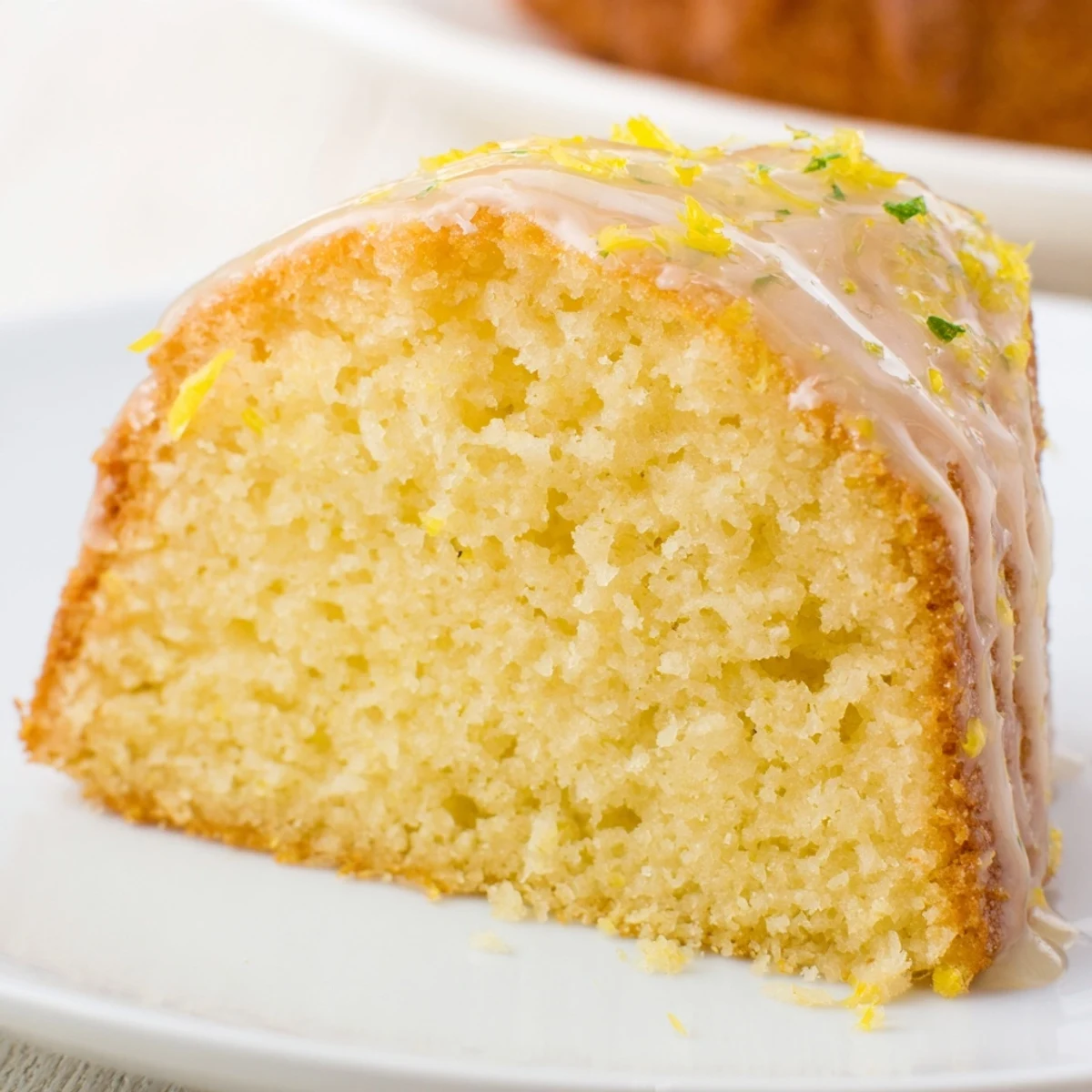 Freshly baked Lemon Drizzle Cake sits on a cooling rack, the glossy, zesty glaze dripping down the golden crust.