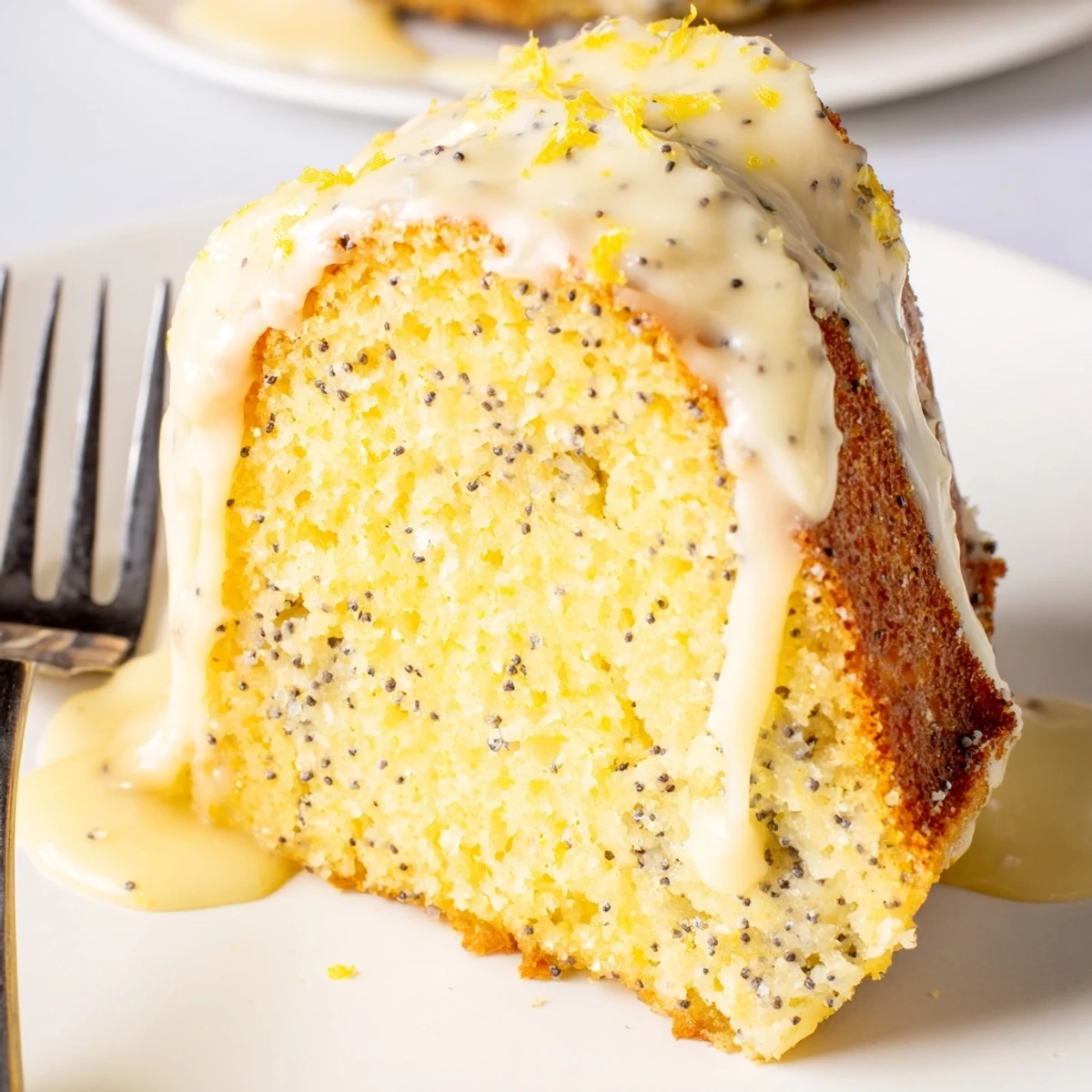 Lemon Poppy Seed Bundt Cake with Lemon Glaze sits on a white platter with fresh lemon slices and tea nearby.