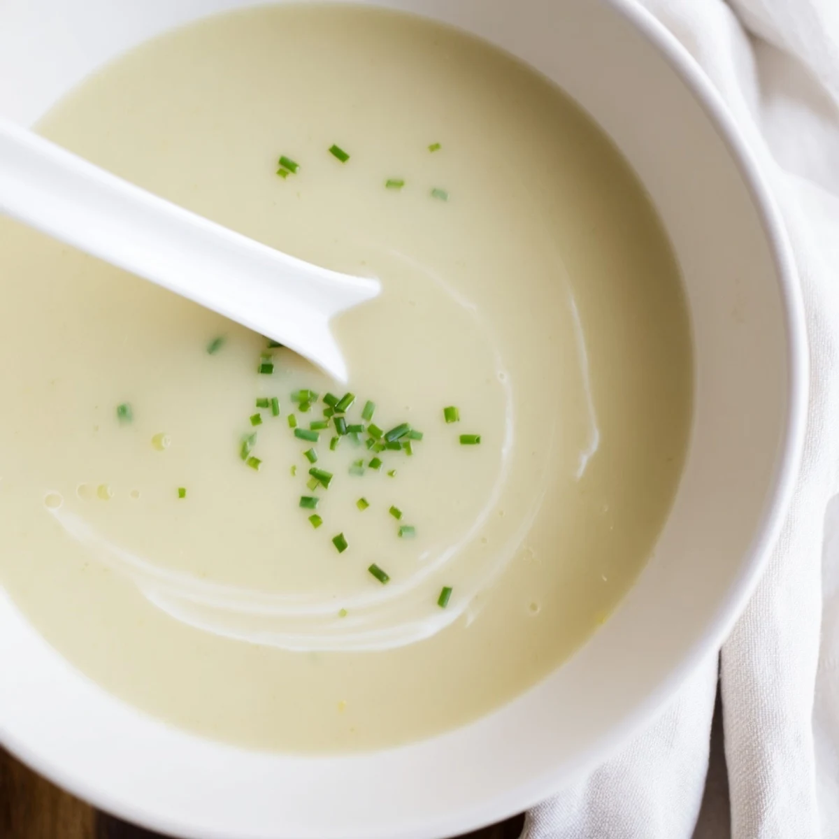 Top-down view of creamy potato leek soup with chives and a side of crusty bread.