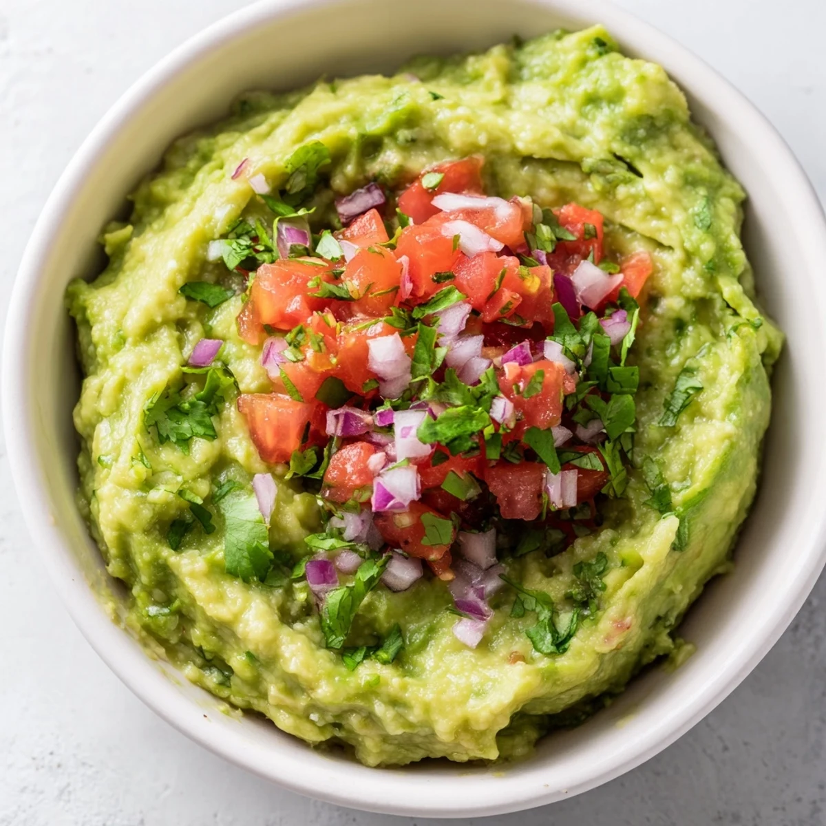Fresh, chunky Game Day Guacamole with Salsa piled high in a serving bowl, surrounded by crispy tortilla chips for dipping.