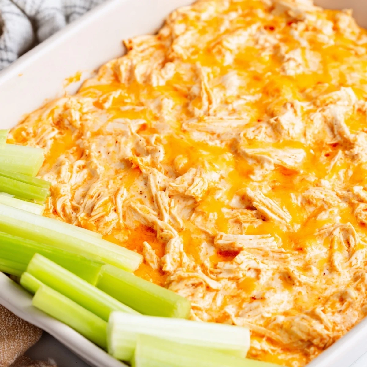 Serving Spicy Buffalo Chicken Dip from a baking dish with celery sticks and ranch on a rustic table.