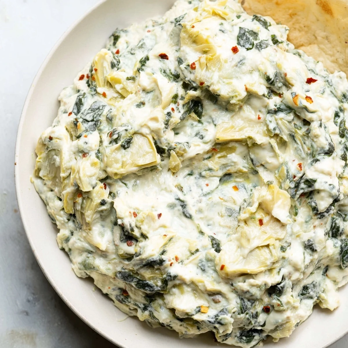 Freshly baked Spinach Dip with Artichokes and Cheese bubbling in a ceramic dish, with a golden, cheesy crust.