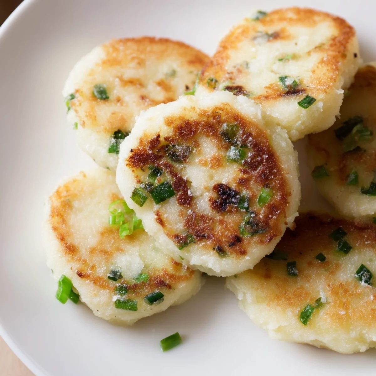 Golden, pan-fried Irish Potato Cakes with Scallions reveal a crispy, golden-brown exterior and tender, scallion-flecked interior on a rustic wooden board.  