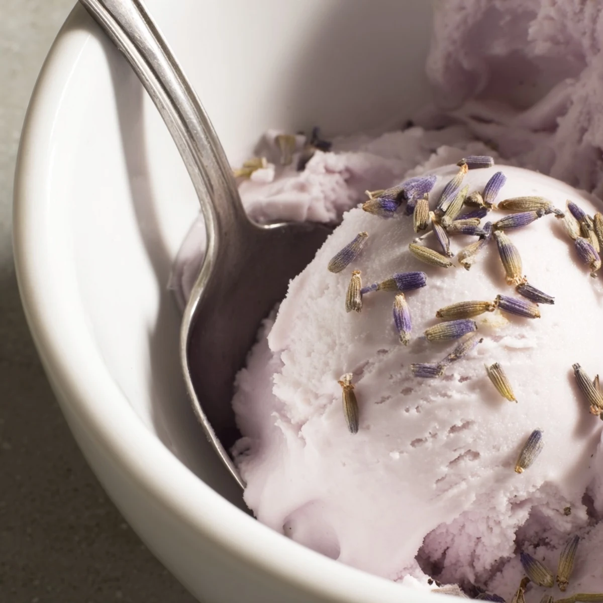 A scoop of lavender ice cream in a waffle cone topped with a fresh berry garnish, ready to serve.