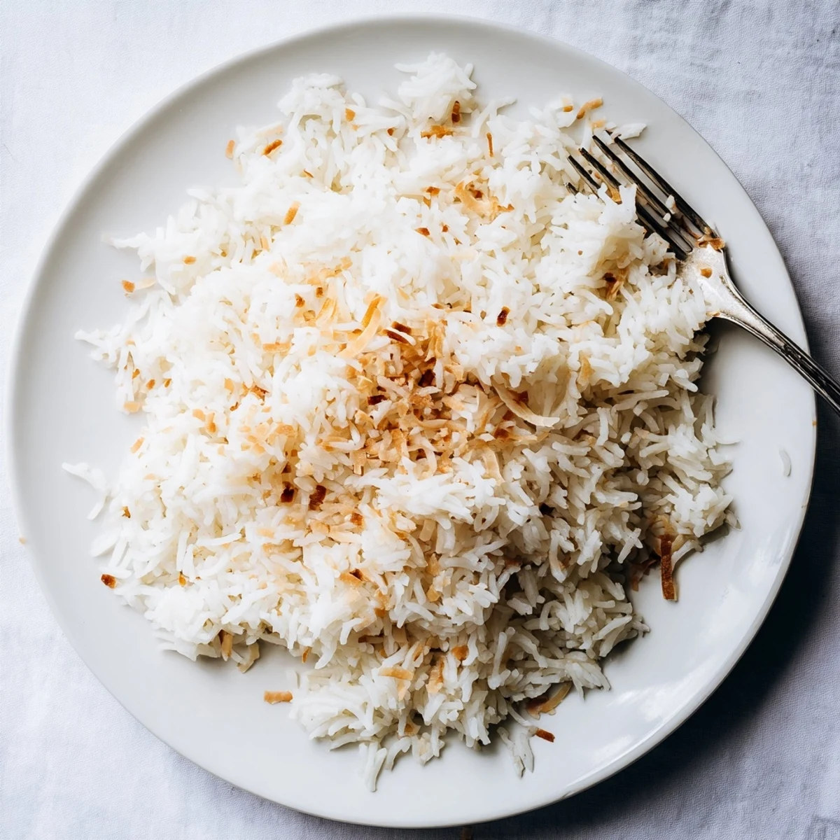 Steaming bowl of The Best Coconut Rice next to a colorful curry dish and lime wedges for a vibrant meal.