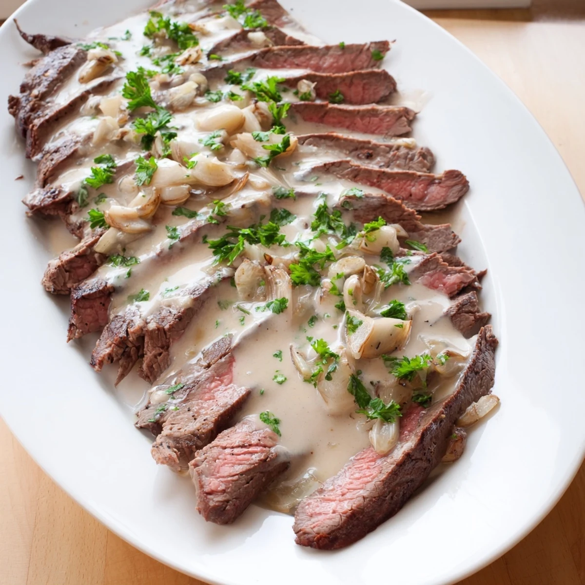 A seared flank steak slices open revealing pink center, drizzled with creamy roasted garlic sauce and parsley garnish.