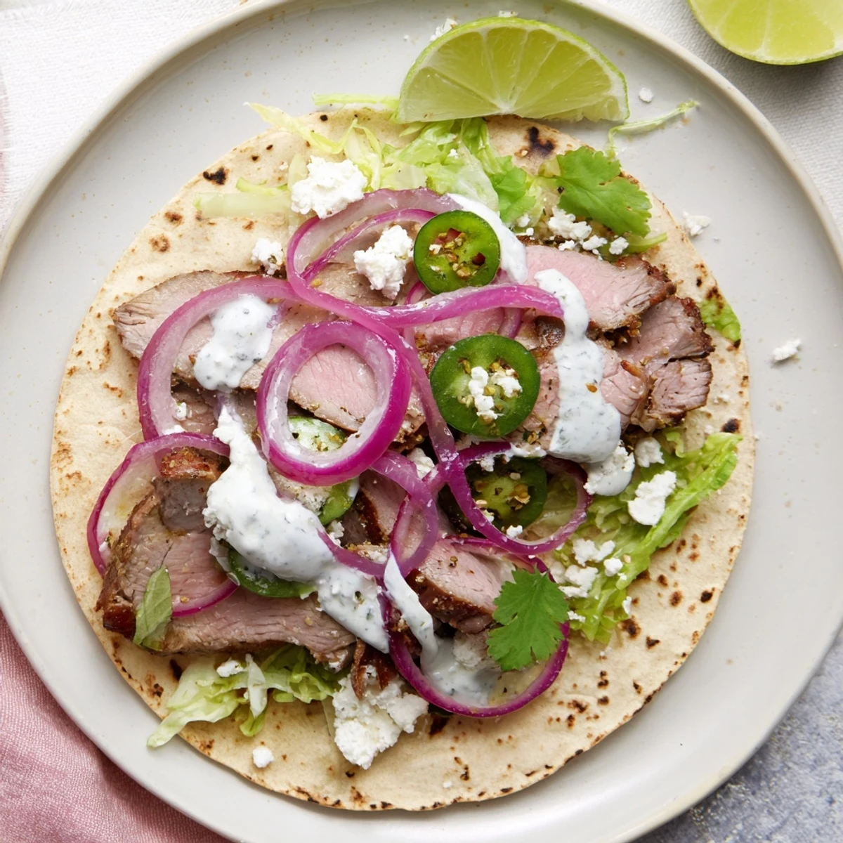 A close-up of cumin crusted leg of lamb with tacos, showing juicy meat with spices, topped with crumbled feta and vibrant shredded lettuce.