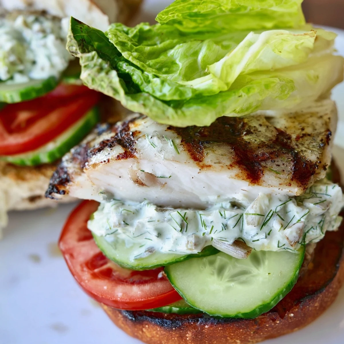 Grilled barramundi fillets stacked on a brioche bun with smoky cos lettuce and vibrant grilled lemon jalapeño tartare sauce.