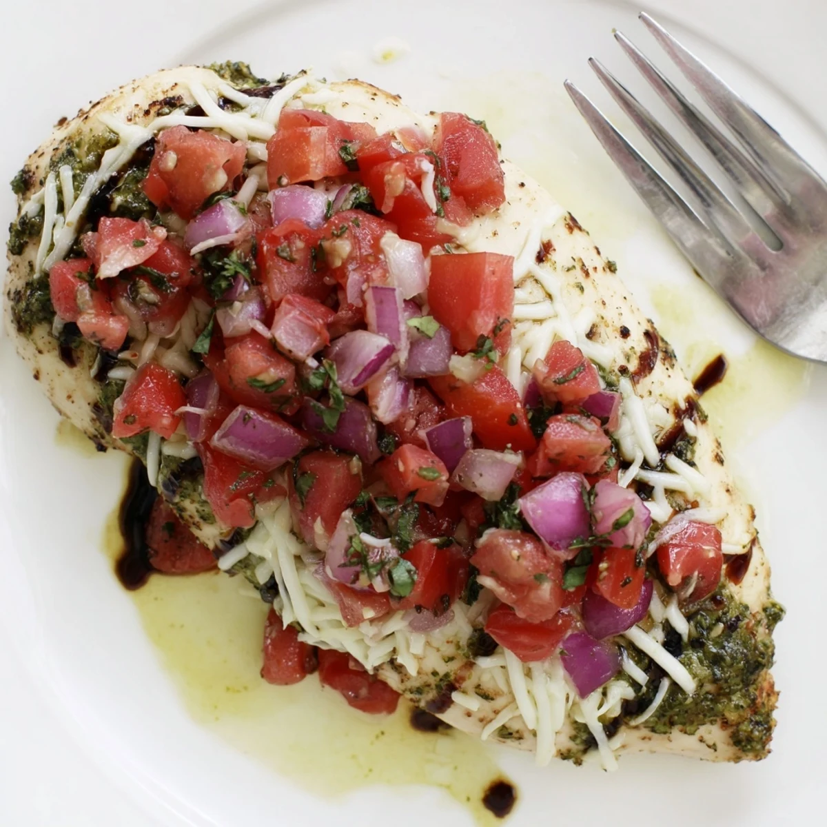 Freshly baked Pesto Bruschetta Chicken with melted mozzarella and vibrant tomatoes on a rustic plate.