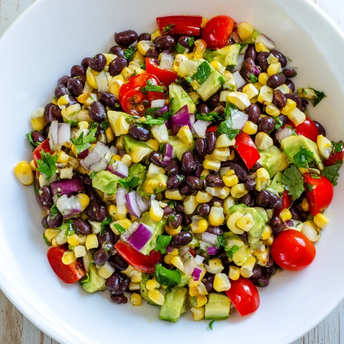 Colorful corn and black bean salad with fresh vegetables in a white bowl