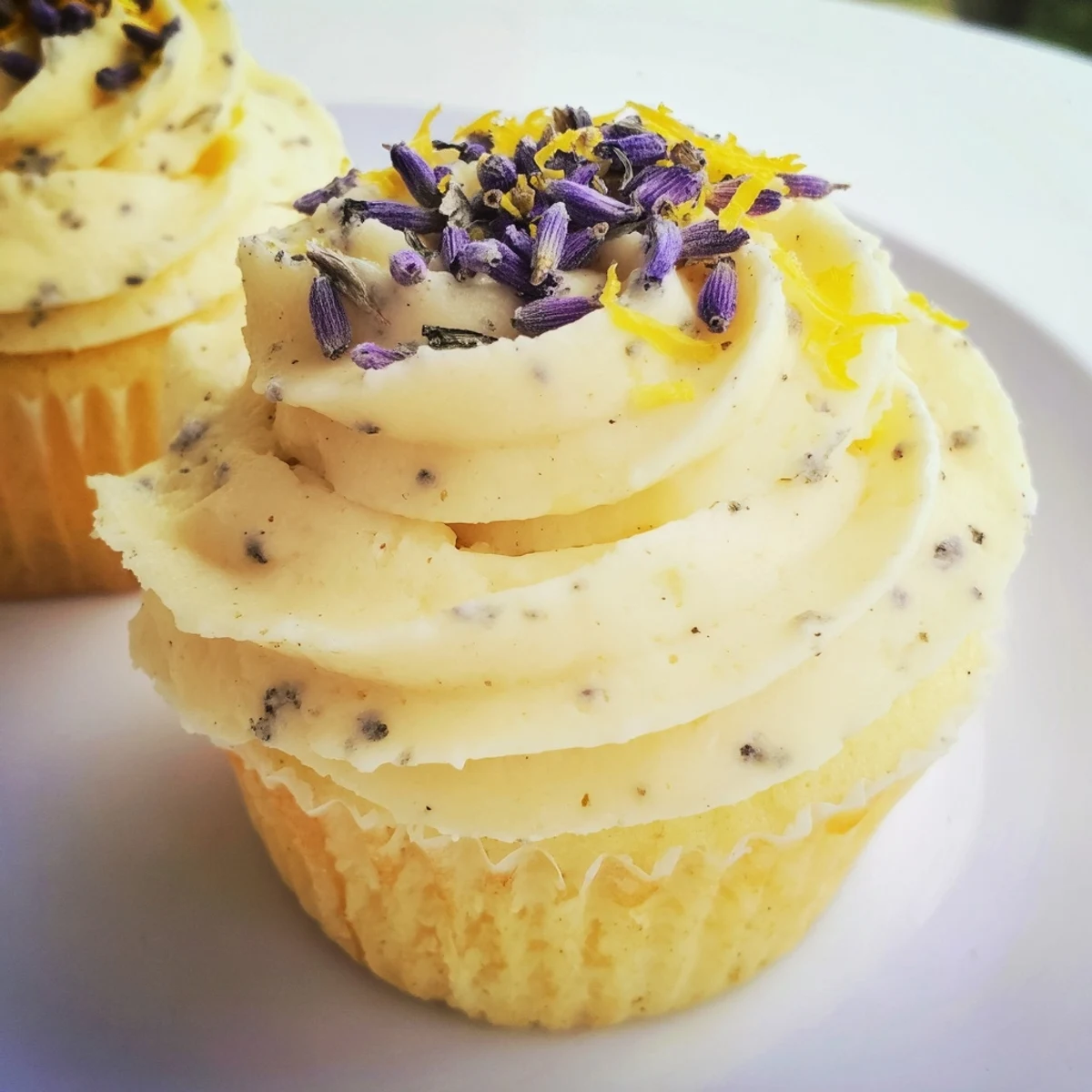 Golden lemon lavender cupcakes with zesty glaze sitting on a white plate garnished with fresh lemon zest