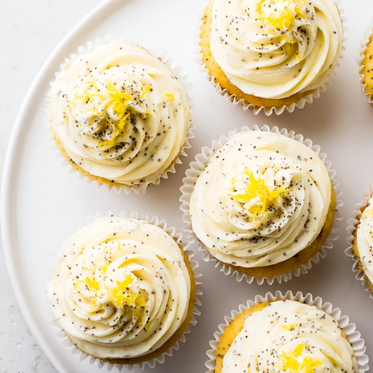 Fluffy homemade lemon poppy seed cupcakes speckled with tiny black seeds and zesty citrus glaze