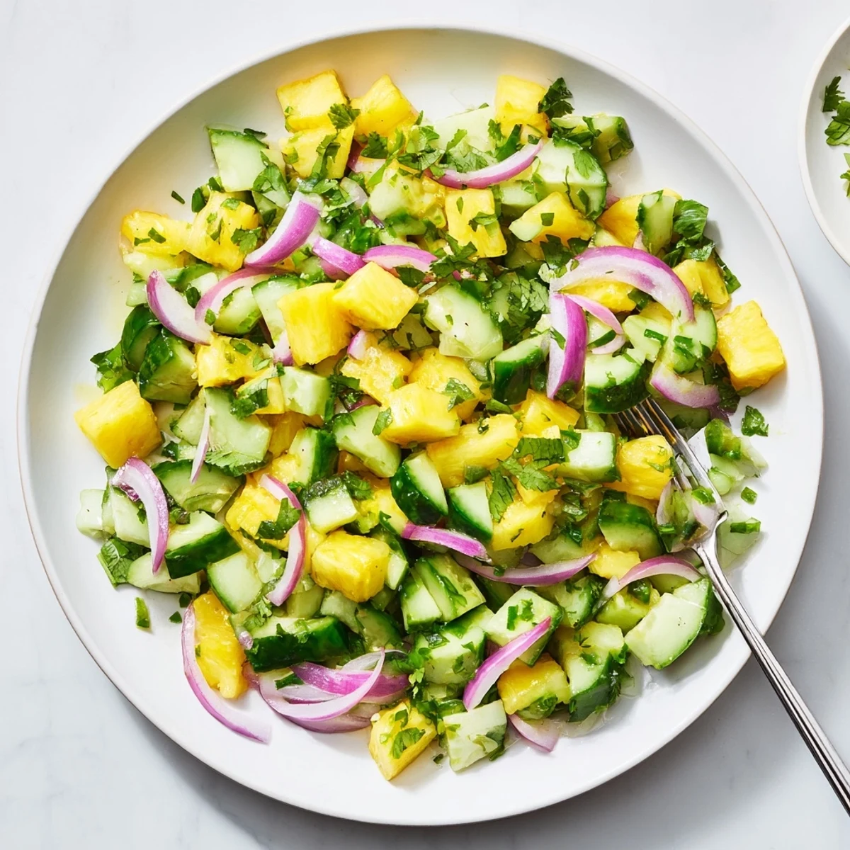 Colorful bowl of pineapple cucumber salad topped with fresh cilantro and lime vinaigrette, a refreshing vegan side dish for summer meals
