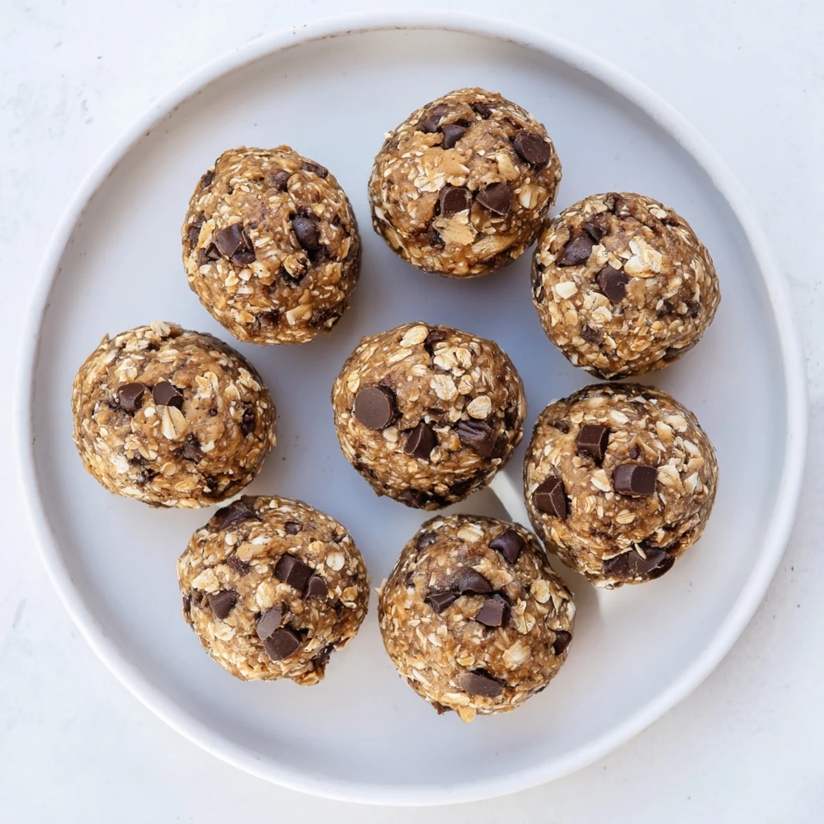 No bake chocolate peanut butter protein balls rolled in mini chocolate chips on a white plate