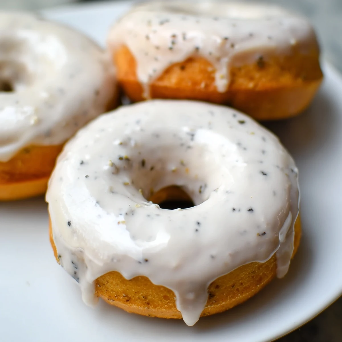 Freshly baked Earl Grey mochi donuts resting on baking parchment their vanilla bean-speckled icing glistening under natural kitchen light