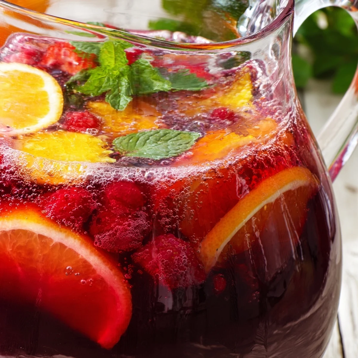 Vibrant pink Love Potion Punch in clear pitcher adorned with fresh mint and berries