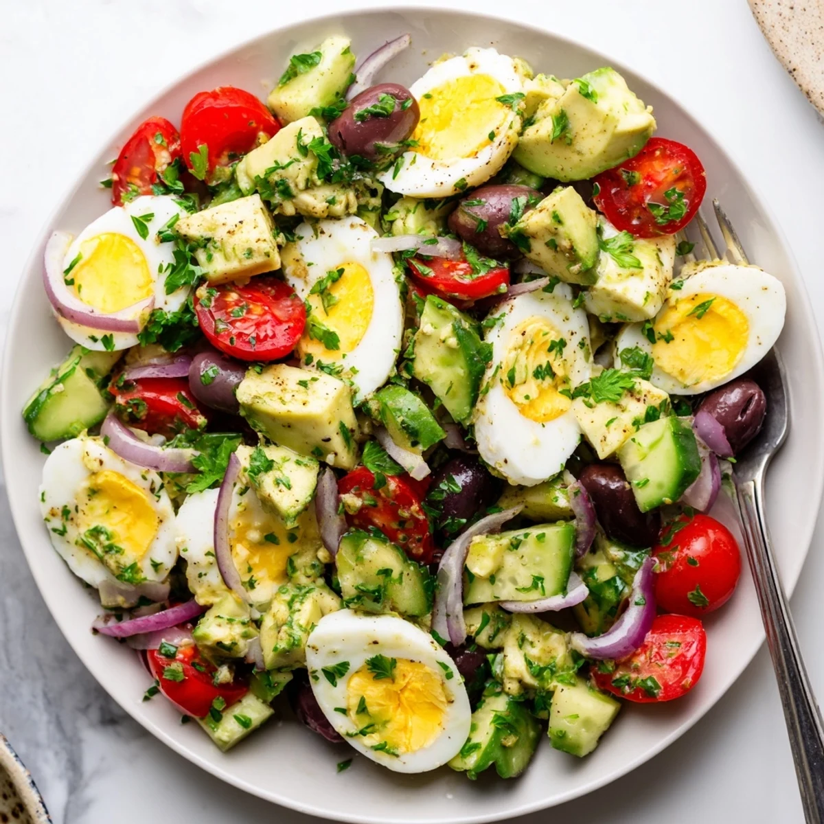 Creamy Mediterranean avocado egg salad served in a white bowl with fresh vegetables and herbs