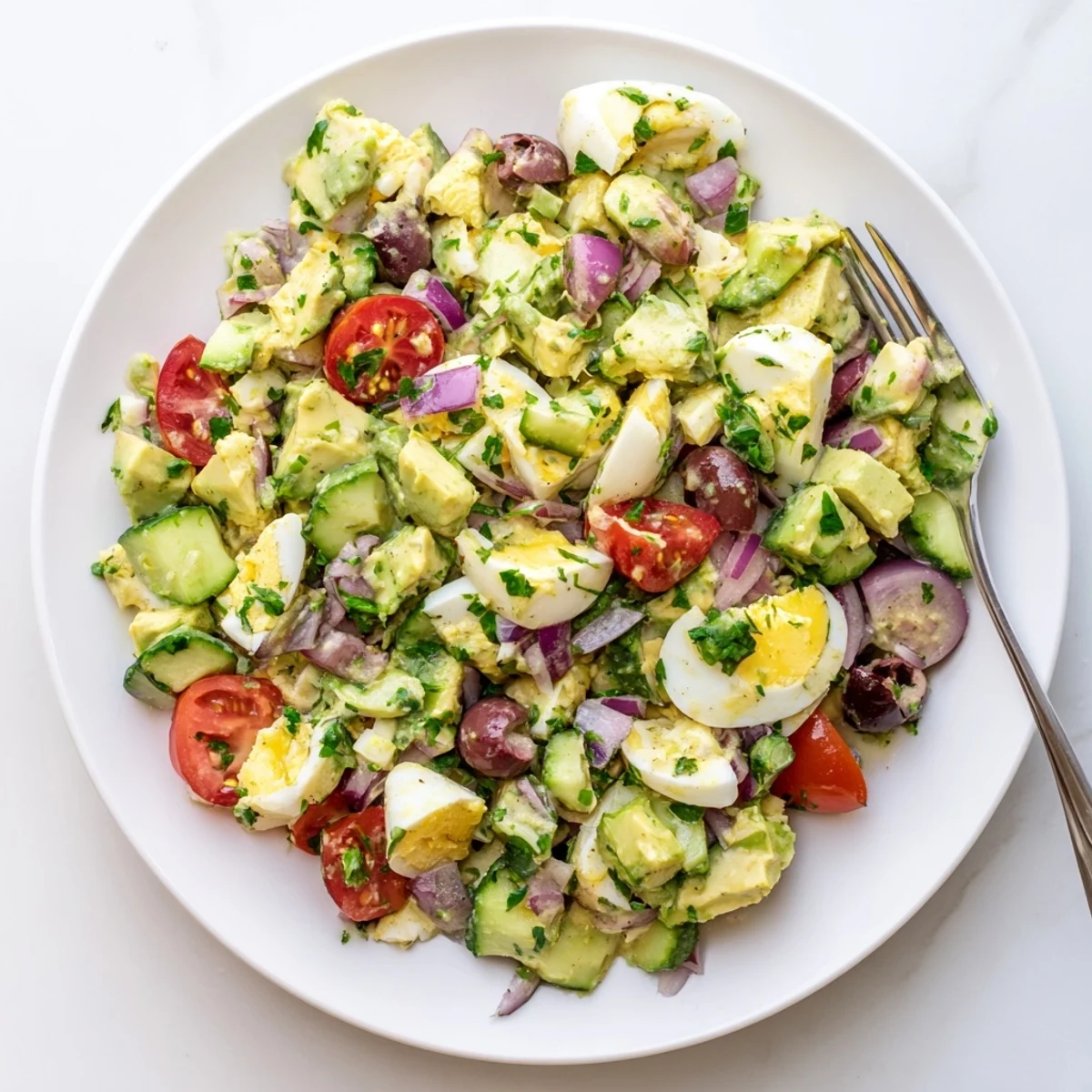 Vibrant bowl of zesty Mediterranean avocado egg salad featuring cherry tomatoes, olives, and parsley