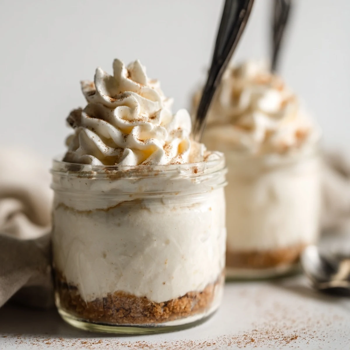 Glass mason jars layered with cinnamon-spiced cheesecake filling and buttery graham cracker base, ready to serve