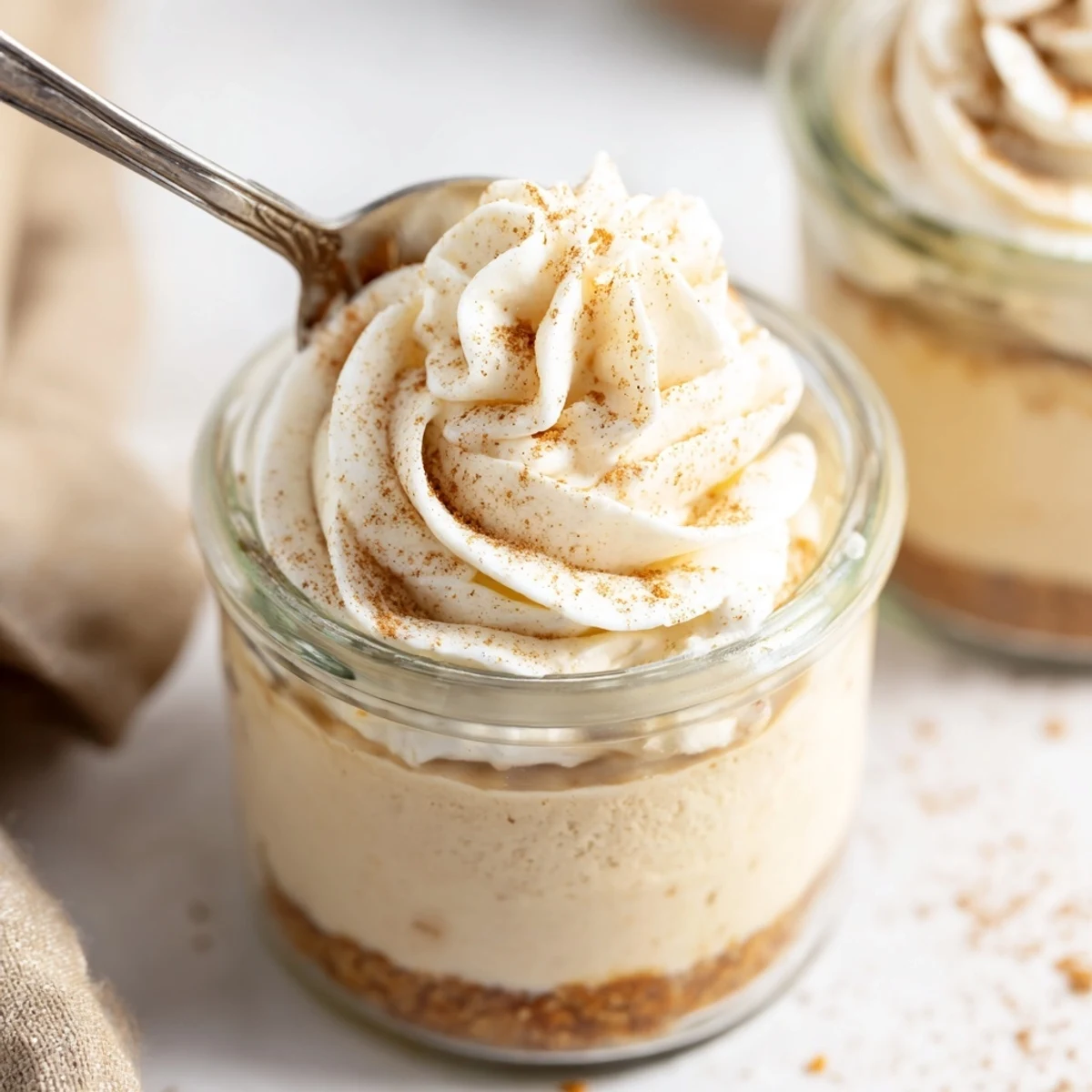 Creamy no bake spiced cheesecakes in portable jars topped with dusted cinnamon and fluffy whipped cream