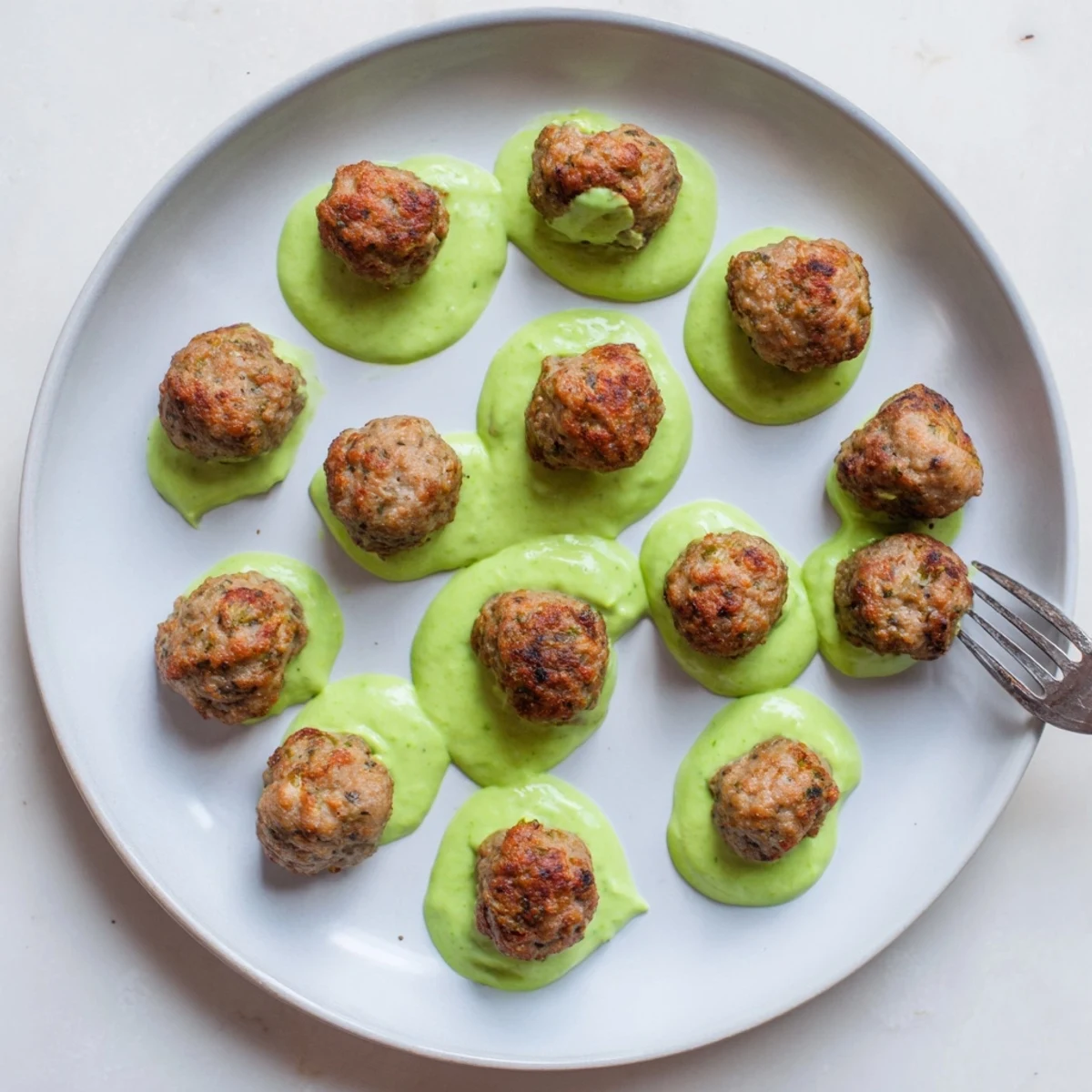 Golden baked salmon meatballs plated with vibrant green creamy avocado sauce for dipping