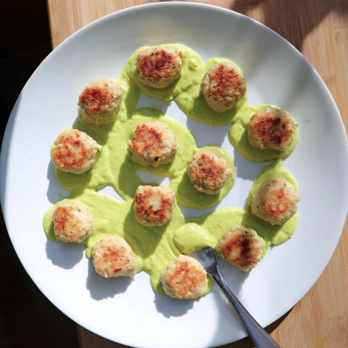 Tender salmon meatballs fresh from the oven with smooth zesty avocado sauce drizzled on top
