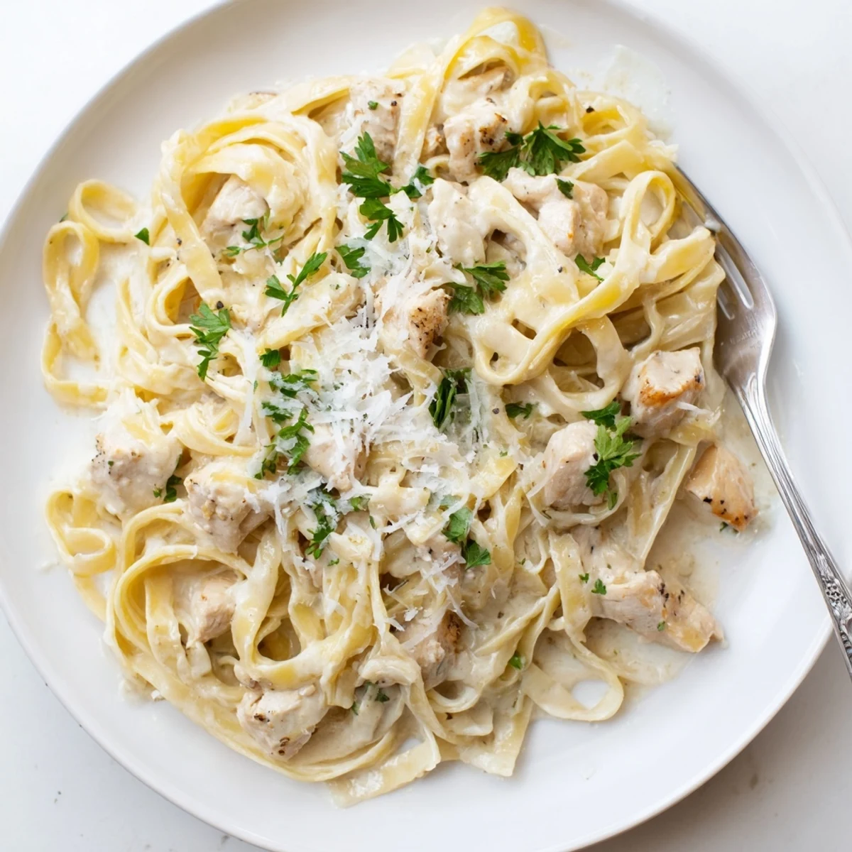 Steaming bowl of creamy garlic Parmesan chicken pasta garnished with green parsley and Parmesan shavings.
