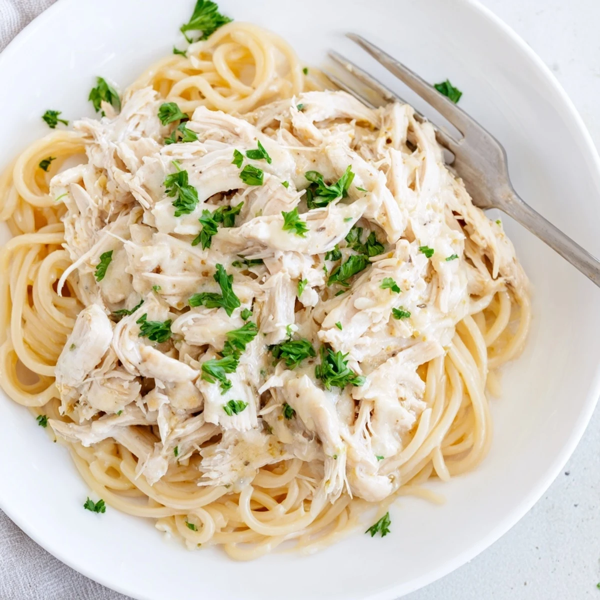 Crock Pot Angel Chicken featuring shredded breasts draped in creamy golden sauce over a bed of delicate angel hair pasta