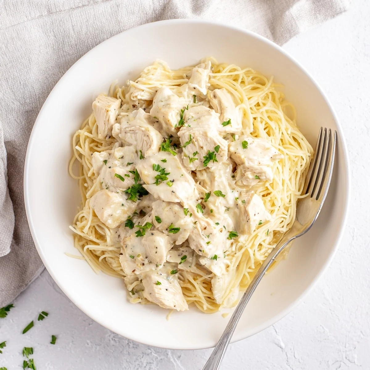 Slow cooker Angel Chicken with tender meat swimming in rich white sauce atop mounds of light pasta strands