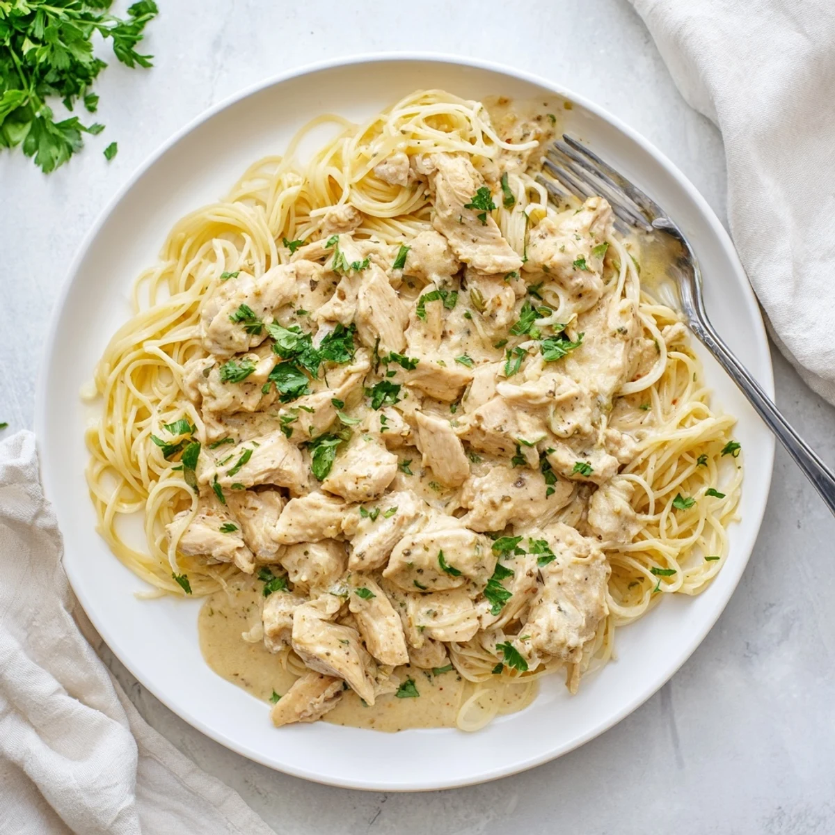 Creamy Crock Pot Angel Chicken dish plated with golden sauce-coated chicken nestled over steaming angel hair pasta garnished with fresh parsley