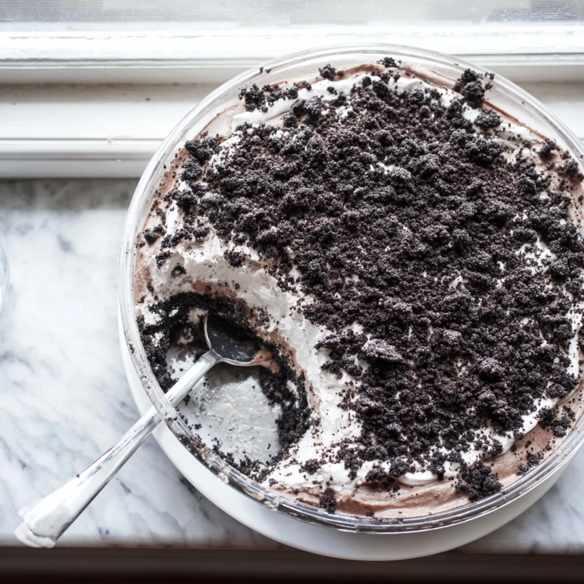 Glass trifle dish showcasing layered keto dirt cake with chocolate crumbs, rich pudding, and fluffy whipped cream topping