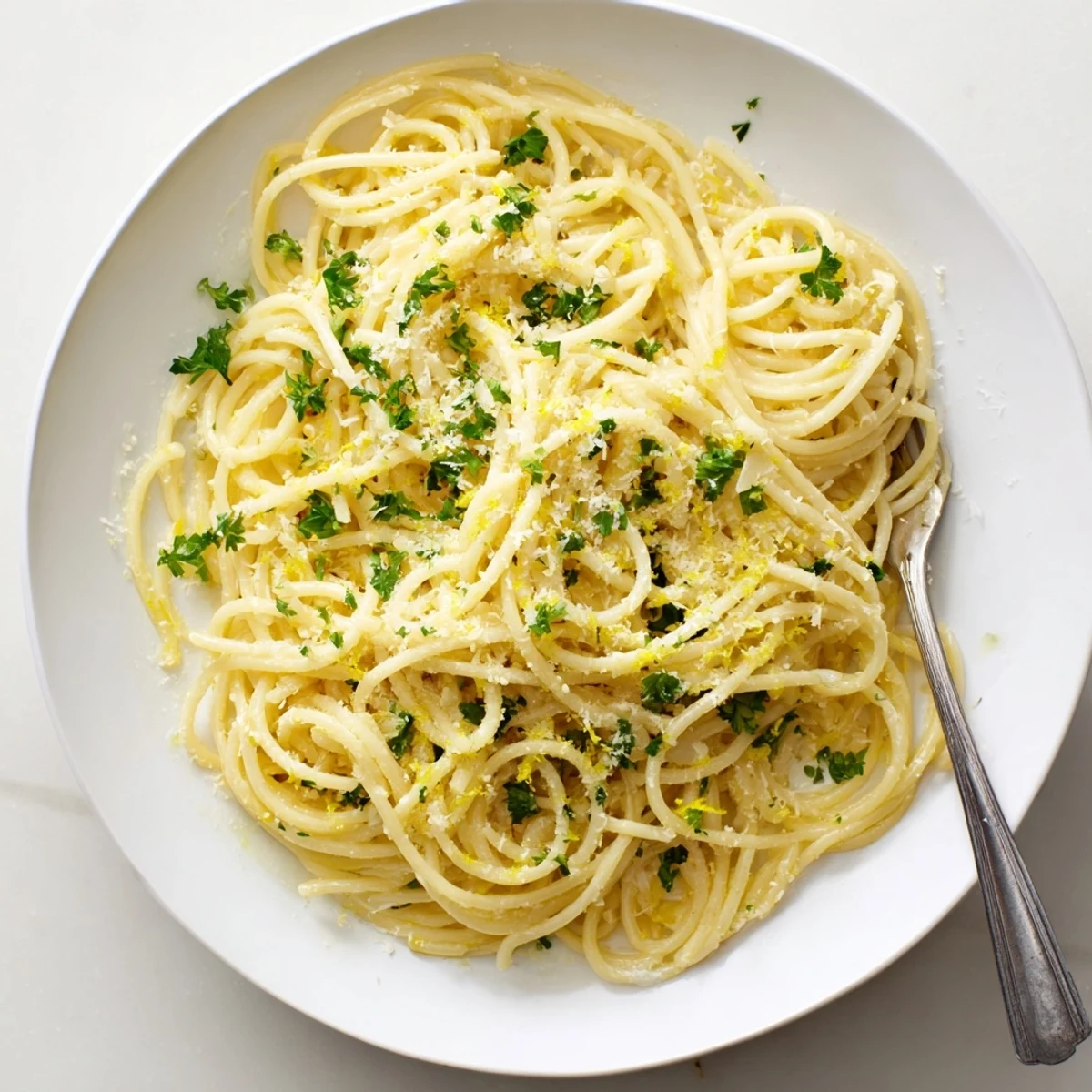 Steaming plate of garlic butter pasta strands coated in glossy sauce with lemon zest garnish