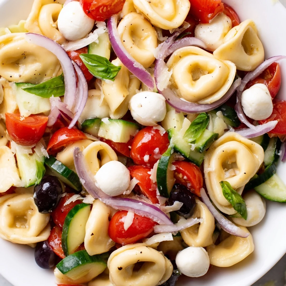 Creamy tortellini salad tossed with cherry tomatoes, cucumber, and zesty Italian dressing in a white bowl