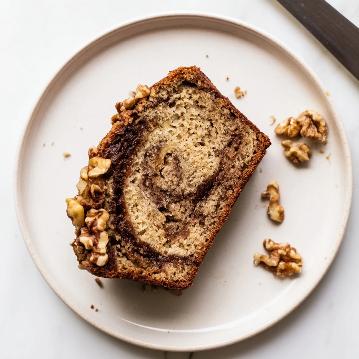 Golden brown banana nut bread loaf sliced to reveal cinnamon swirl and chopped walnuts