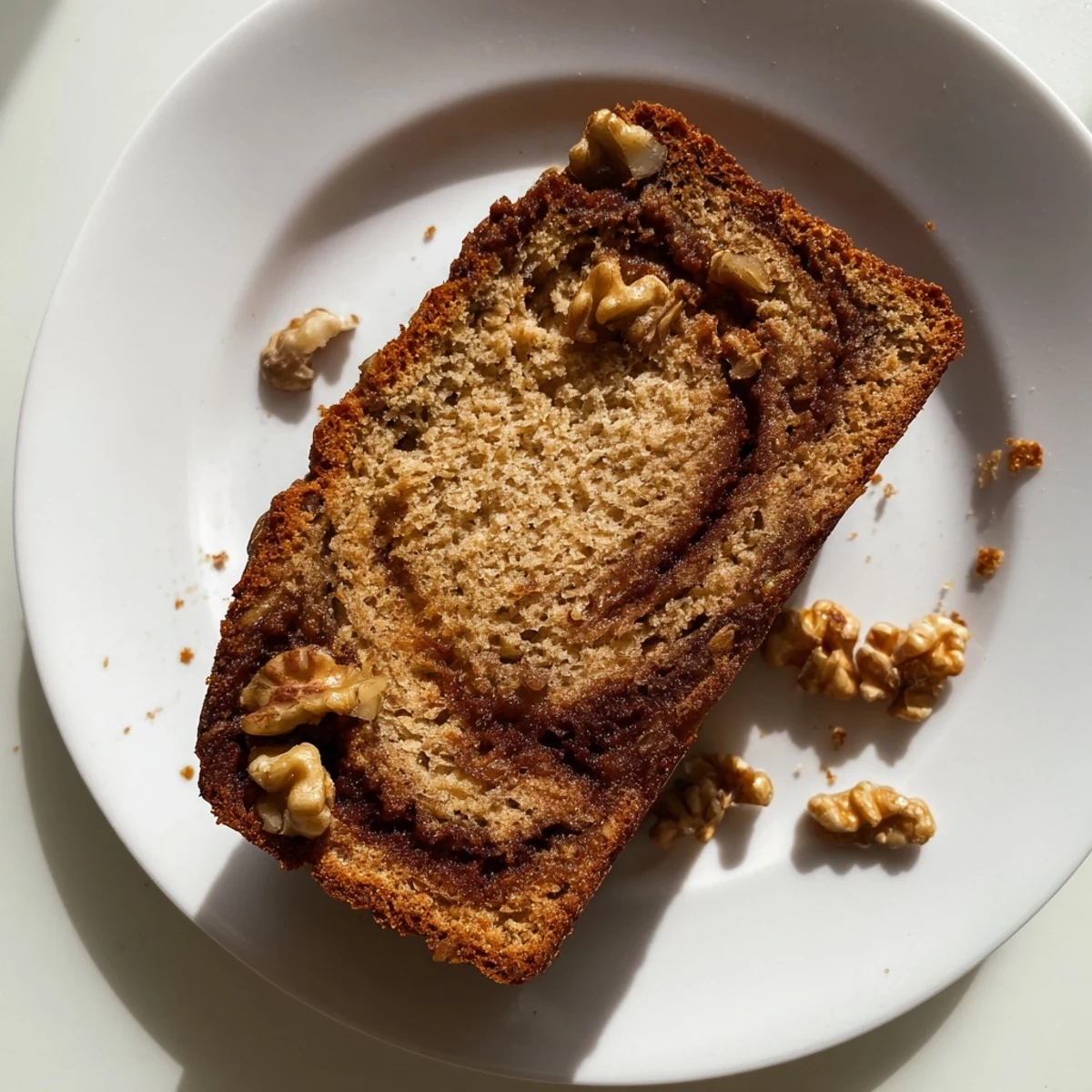 Moist banana bread with walnuts and cinnamon sugar marbling on a white serving plate