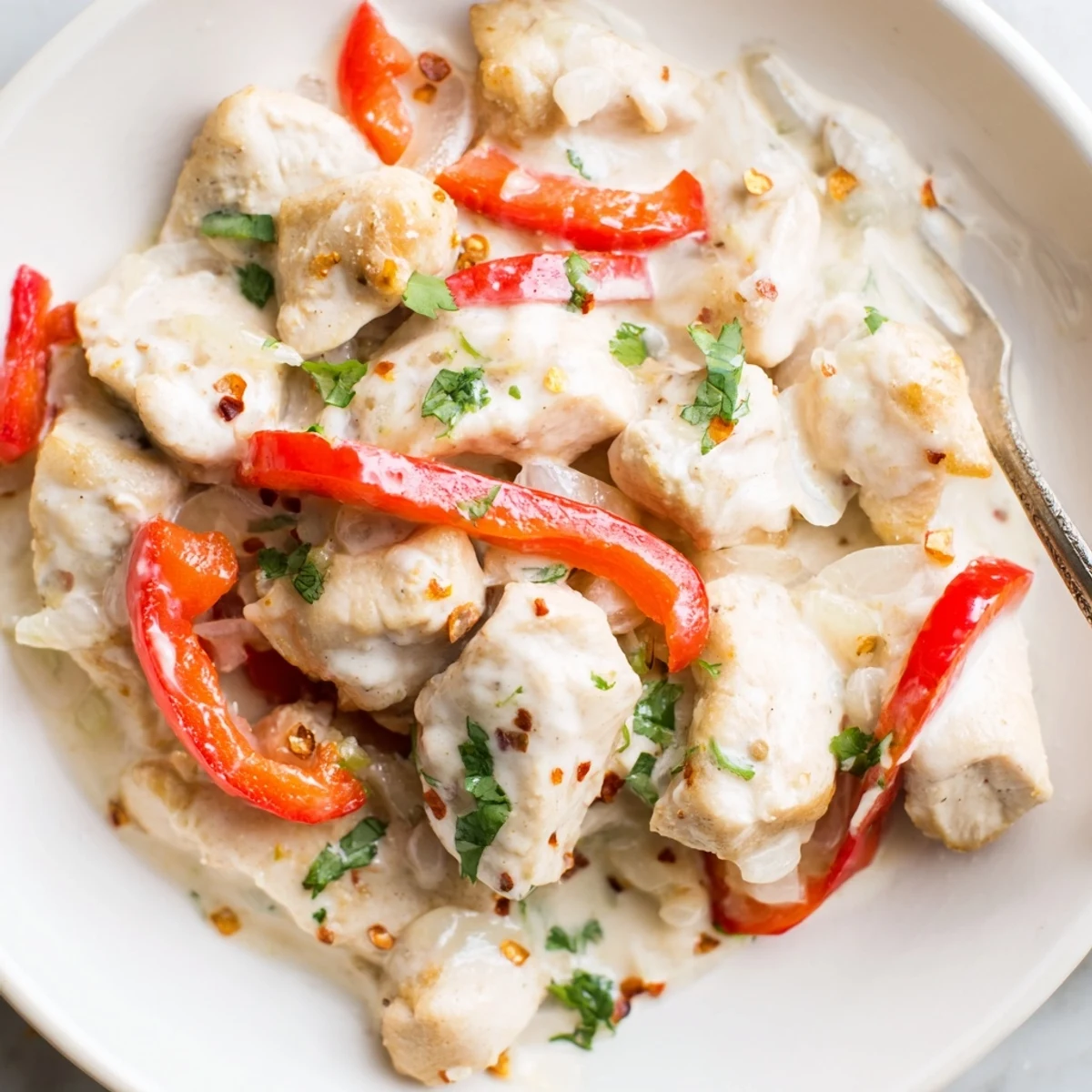 Golden Brazilian coconut chicken pieces simmered in creamy white sauce with red bell pepper and fresh cilantro garnish