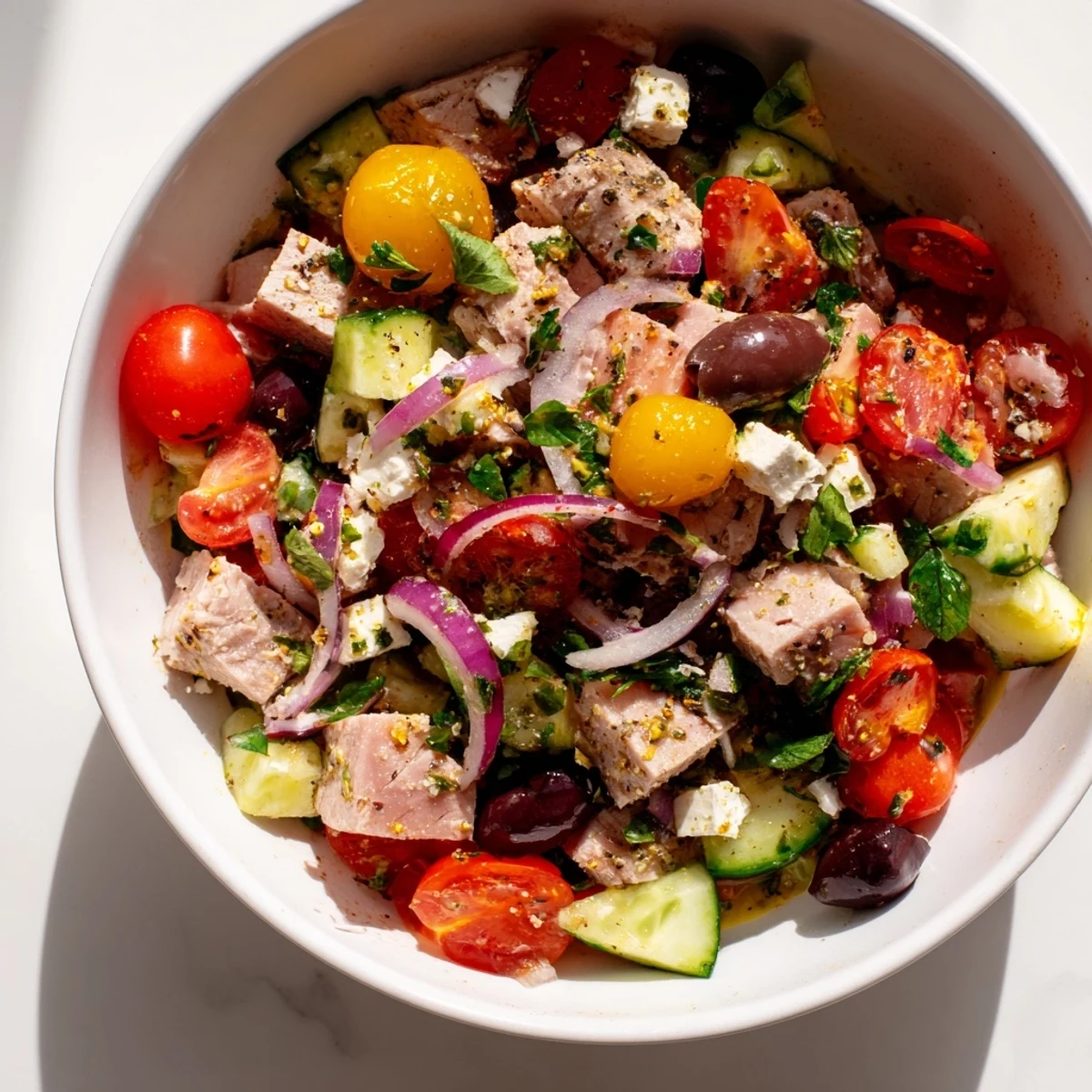 Fresh Mediterranean tuna salad with colorful vegetables, olives, and zesty lemon dressing in a white bowl.
