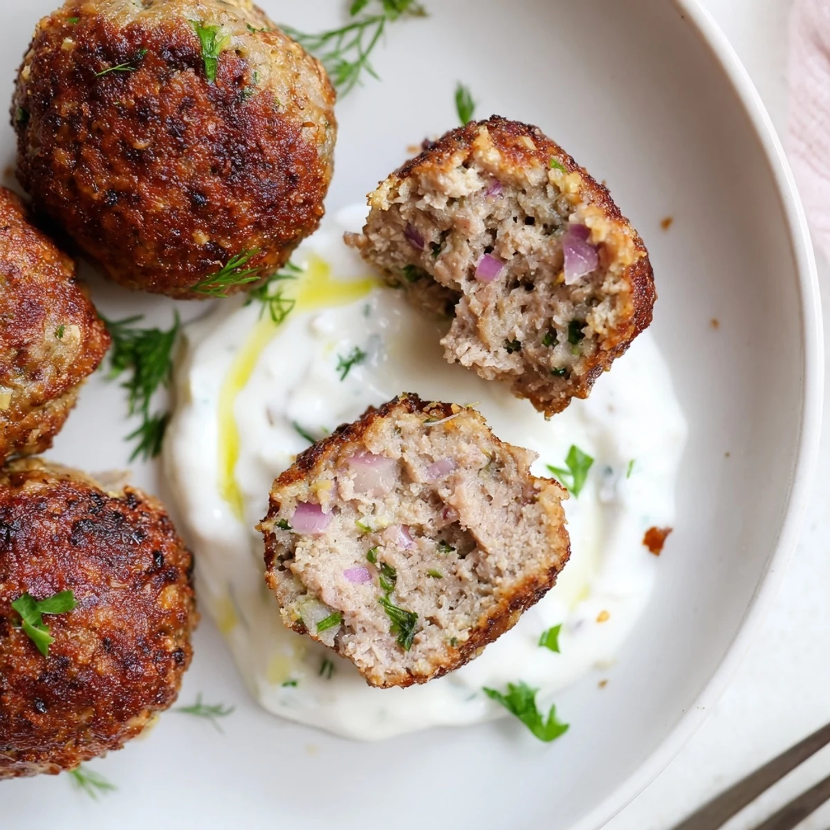 Juicy Greek Style Beef Meatballs plated beside bright dill-yogurt sauce and lemon