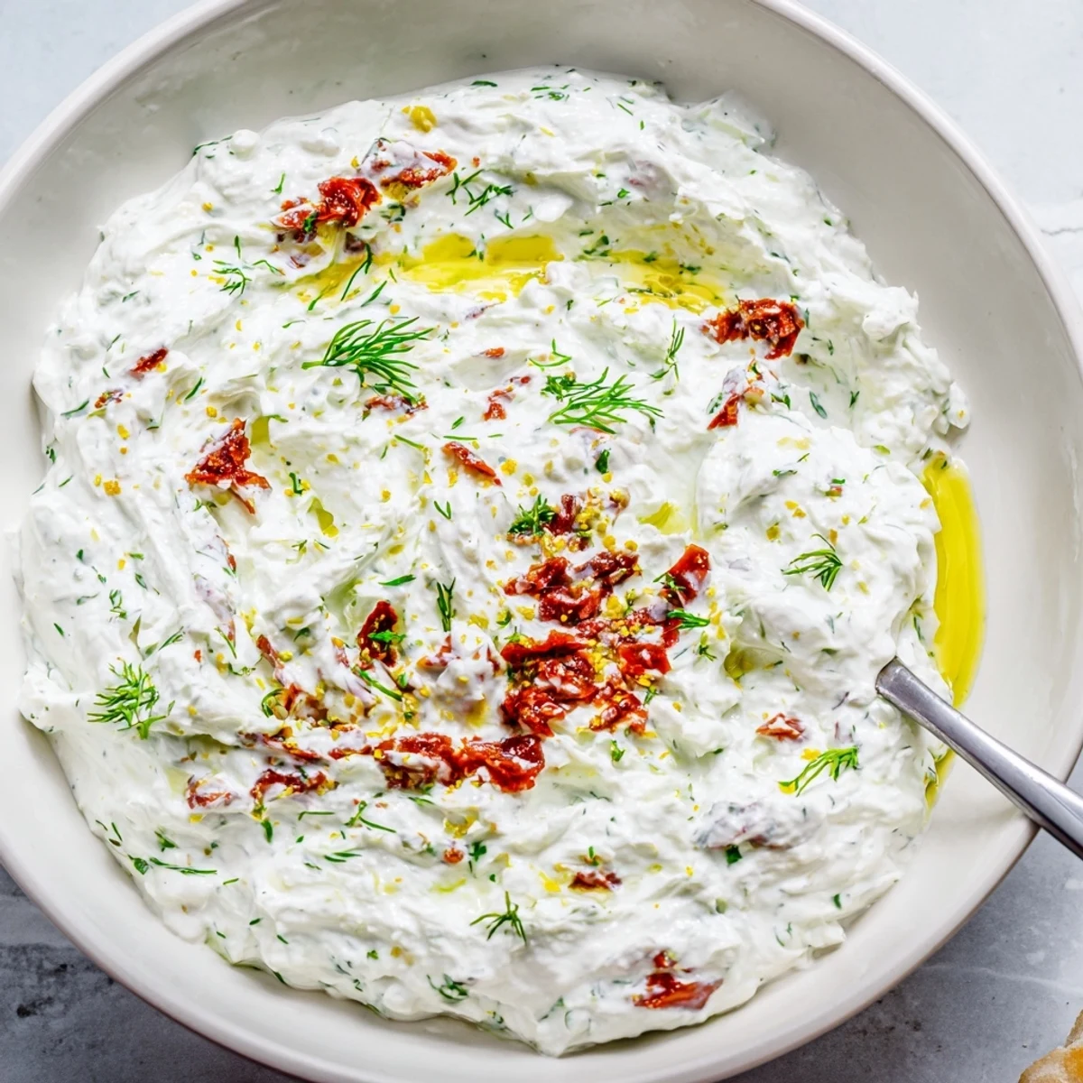 Rustic serving of Creamy Sun Dried Tomato Tzatziki garnished with olive oil drizzle.