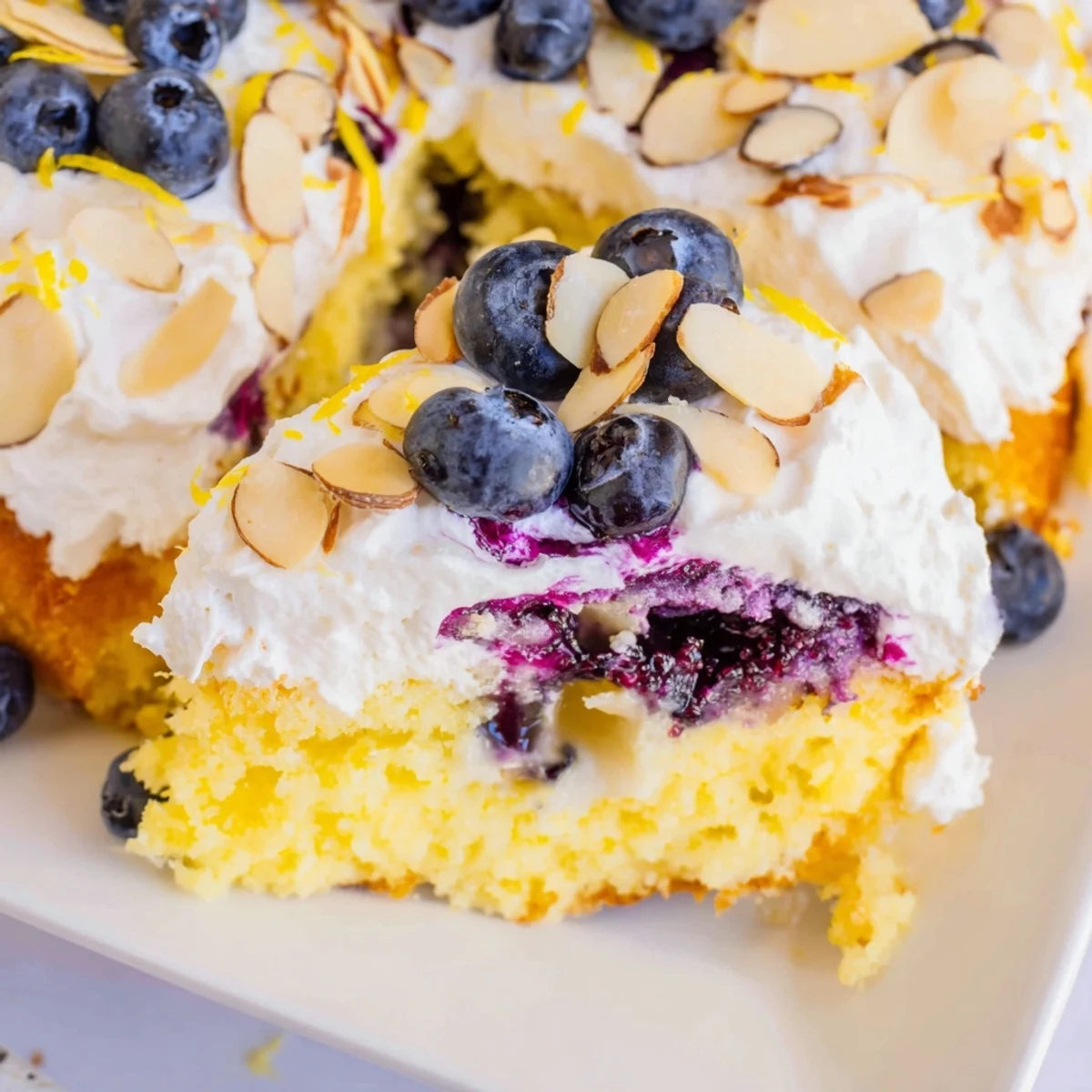Creamy whipped frosting covers this lemon blueberry poke cake sprinkled with browned sliced almonds