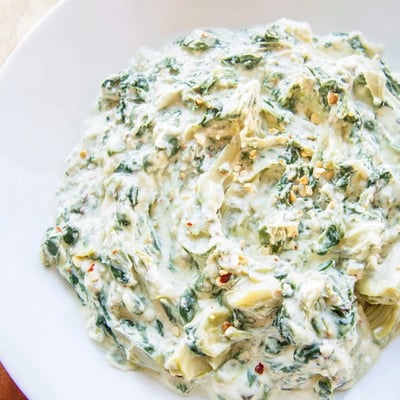 Creamy Spinach Dip with Artichokes and Cheese served warm from the oven, ready for dipping with crunchy crackers.