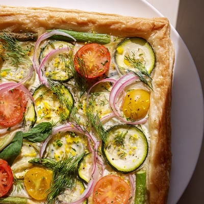 Slices of the flaky Spring Vegetable Tart with Puff Pastry are arranged on a white plate, revealing layers of fresh vegetables and herbs for a light lunch.