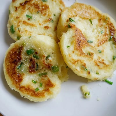 Steam rises from a plate of freshly cooked Irish Potato Cakes with Scallions, served with melting butter and a sprinkle of fresh chives.  